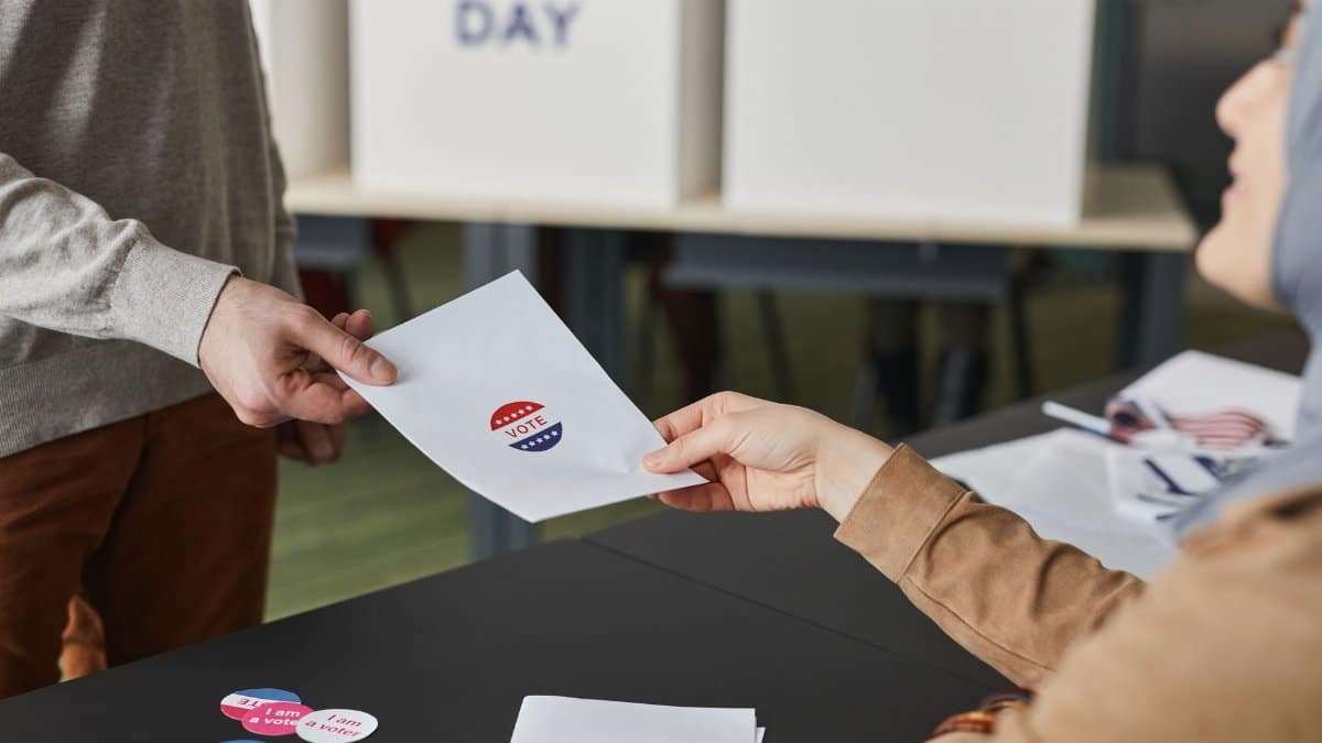 Two people exchanging a ballot paper during an indoor voting process.