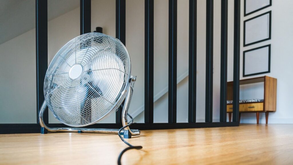 A sleek electric fan placed on a wooden floor in a modern indoor setting, providing comfort and cooling.