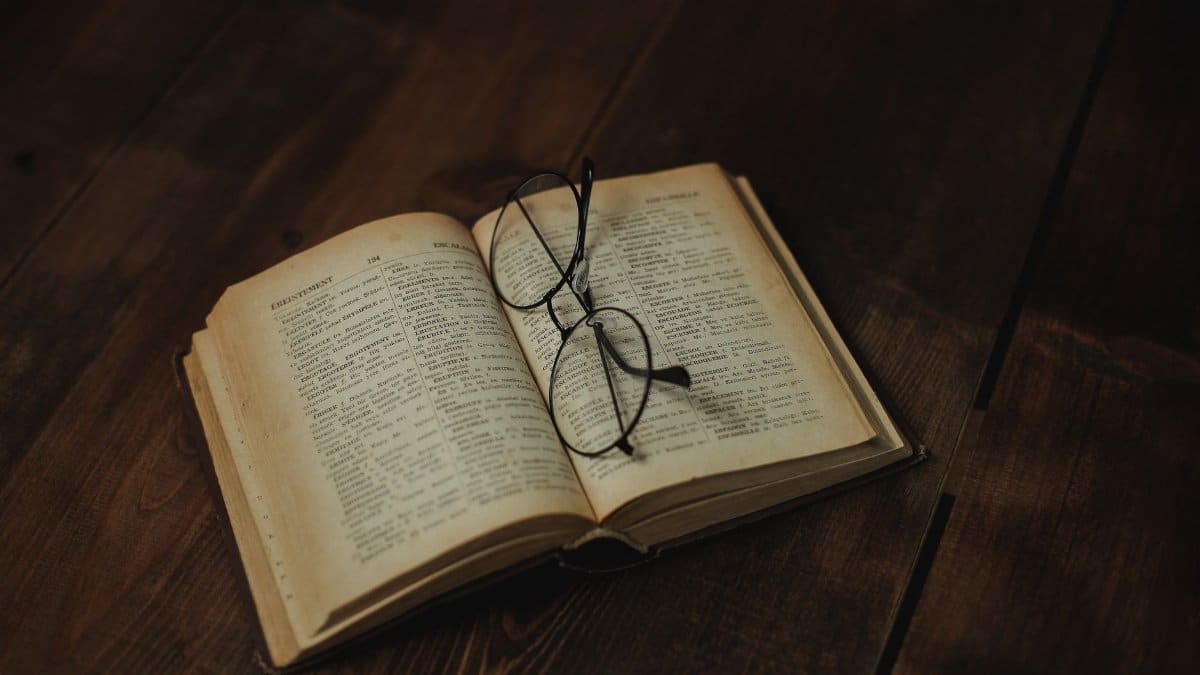 Open vintage book with eyeglasses resting on a wooden surface, evoking a sense of nostalgia.