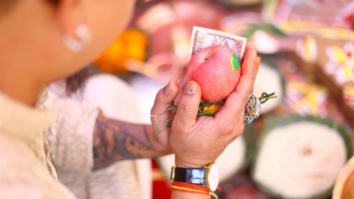 Close-up of hands holding an apple and currency, symbolizing a ceremonial offering.