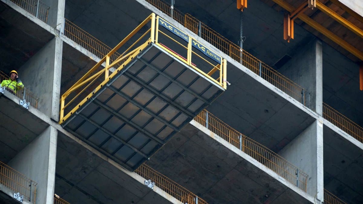 A construction worker supervises a platform lift at a high-rise building site.