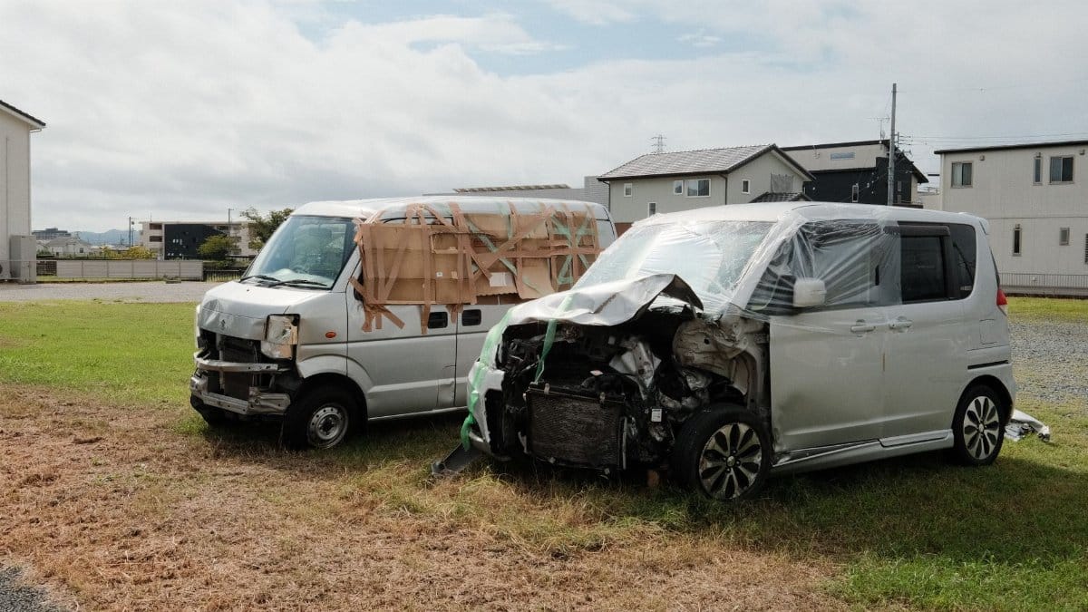 Two wrecked vans parked on a grassy area in Toyokawa, Japan.