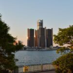 Scenic view of the Detroit Renaissance Center with lush trees framing the skyline at sunset.