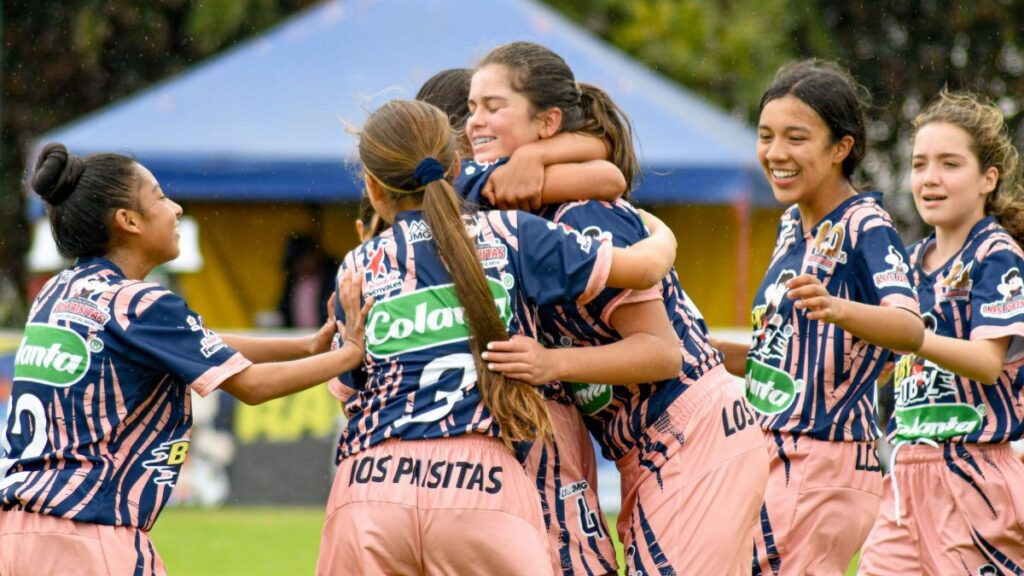 Teenage girls' soccer team celebrating a victory on the field outdoors.