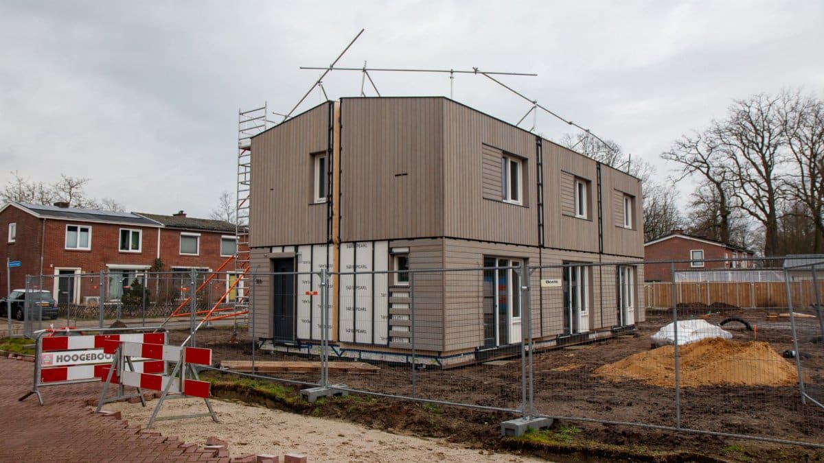 A modern house under construction with scaffolding, fences, and construction signs on a cloudy day.