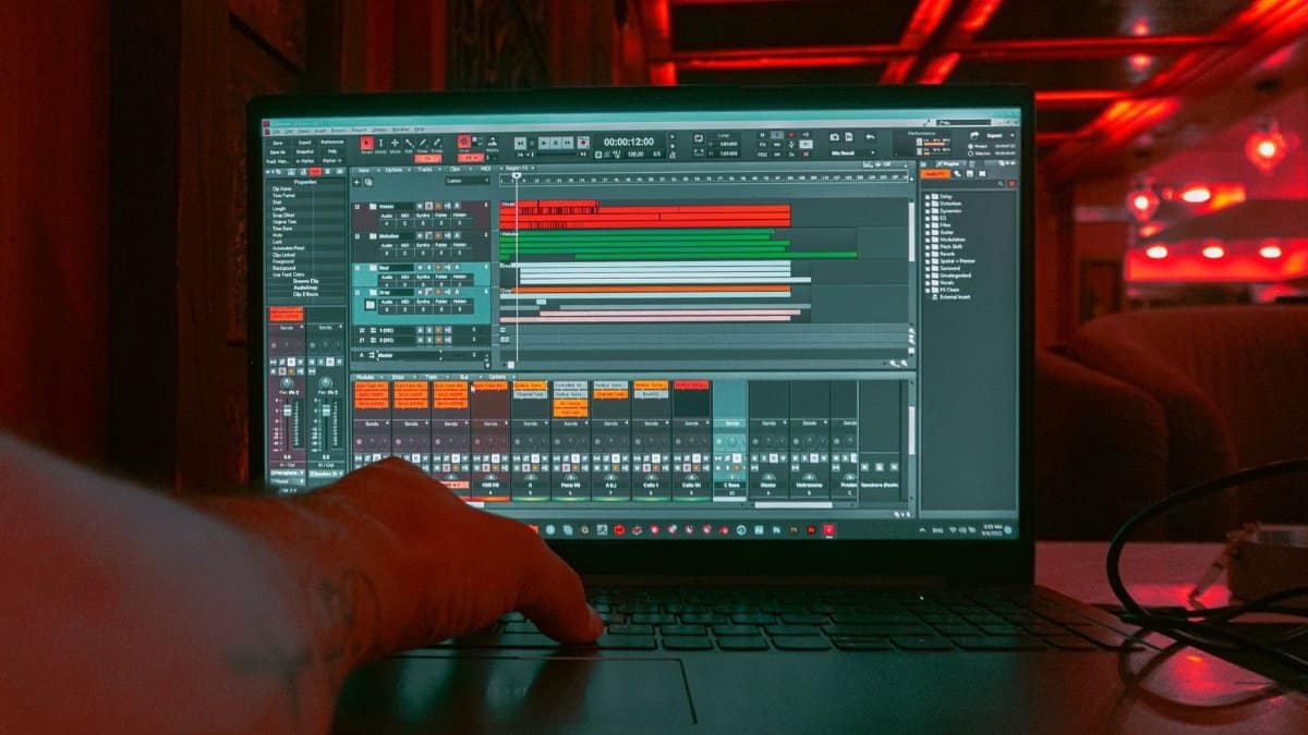 A person editing audio tracks on a laptop indoors with a red ambient lighting background.