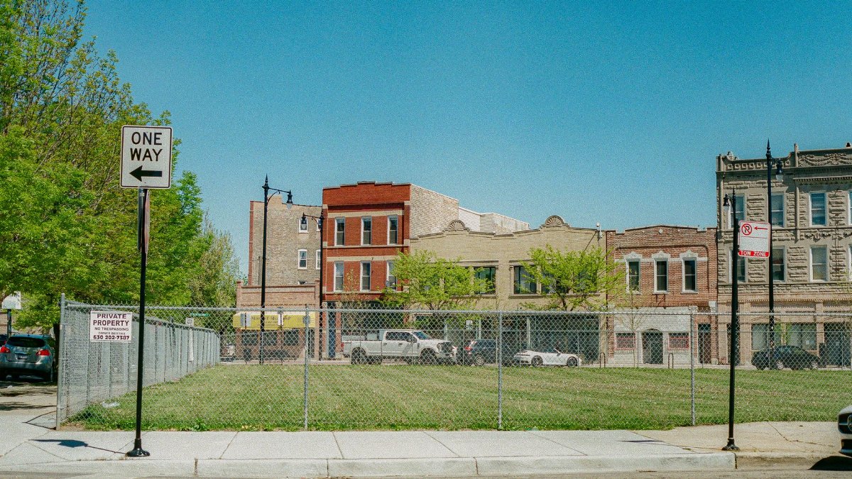 A street view in Chicago showing a vacant lot with surrounding buildings and clear blue sky.