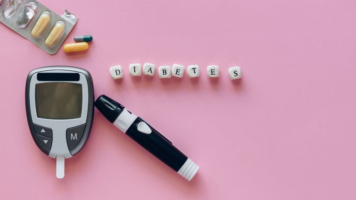 Close-up of diabetes management tools including glucometer and pills on a pink background.