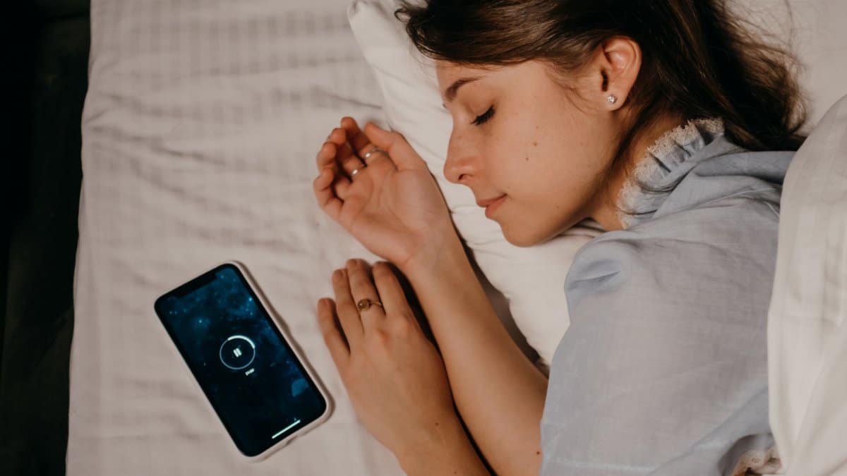 A woman peacefully sleeps in bed with a smartphone beside her, illustrating modern bedtime habits.