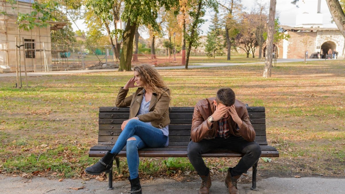 An upset couple seated on a park bench, expressing frustration during an autumn day.