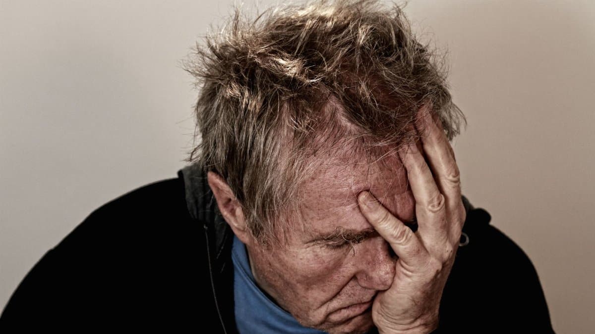 Portrait of an elderly man feeling stress and disappointment, holding his head in his hands.