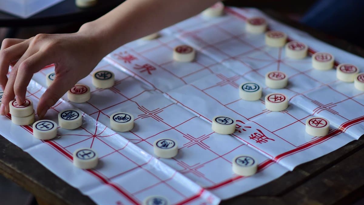A hand strategically moves a piece on a Chinese chess board, showcasing traditional strategy game play.