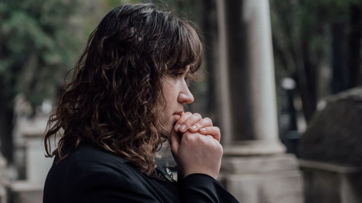 A woman in a cemetery expressing grief and contemplation in a serene outdoor setting.