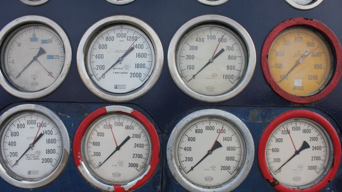 Close-up of multiple industrial pressure gauges on a blue metal panel, showing various readings.
