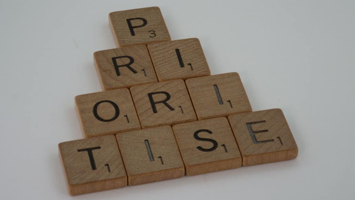 Close-up of wooden Scrabble tiles spelling 'prioritise' on a white surface, set in a pyramid shape.