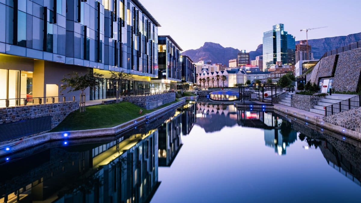 Stunning view of modern buildings reflecting on a canal in Cape Town at twilight.