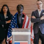 Diverse group of political candidates standing with American flag at voting podium.