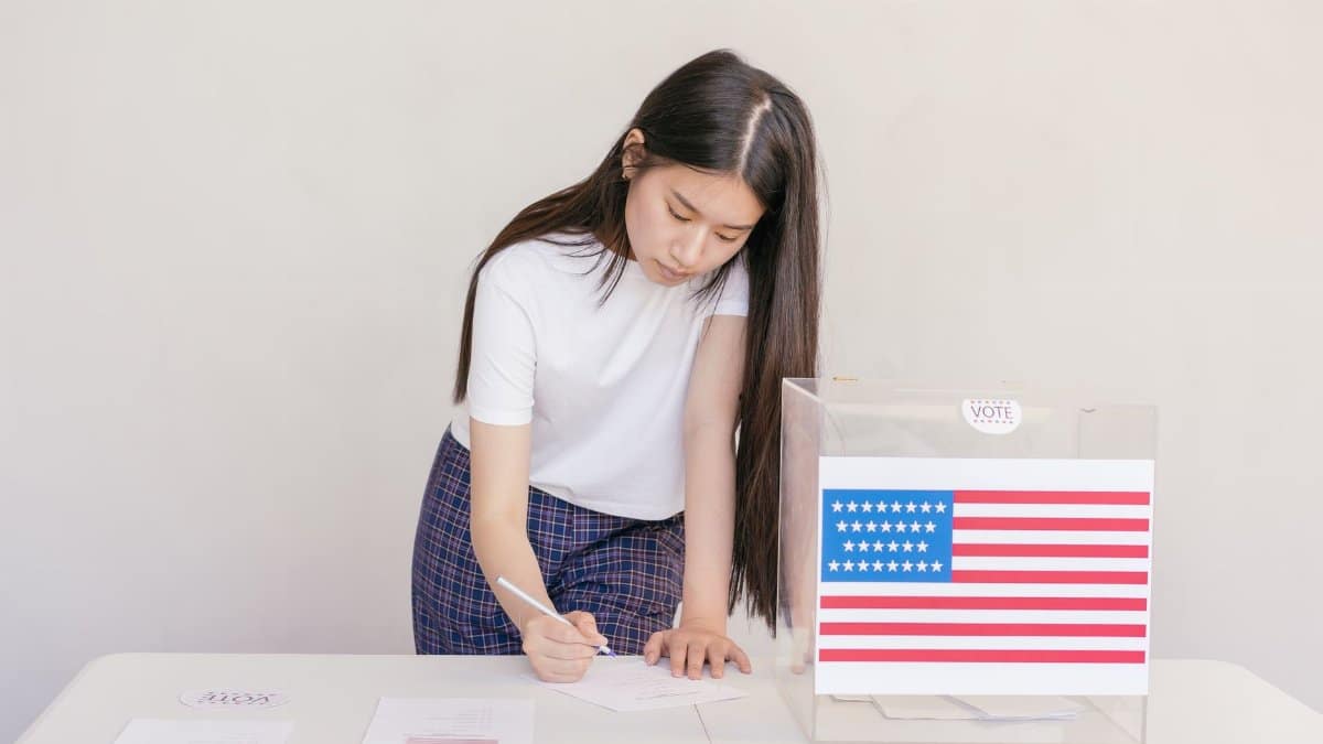 Woman voting in an election, writing down her choice at a ballot box with the American flag.
