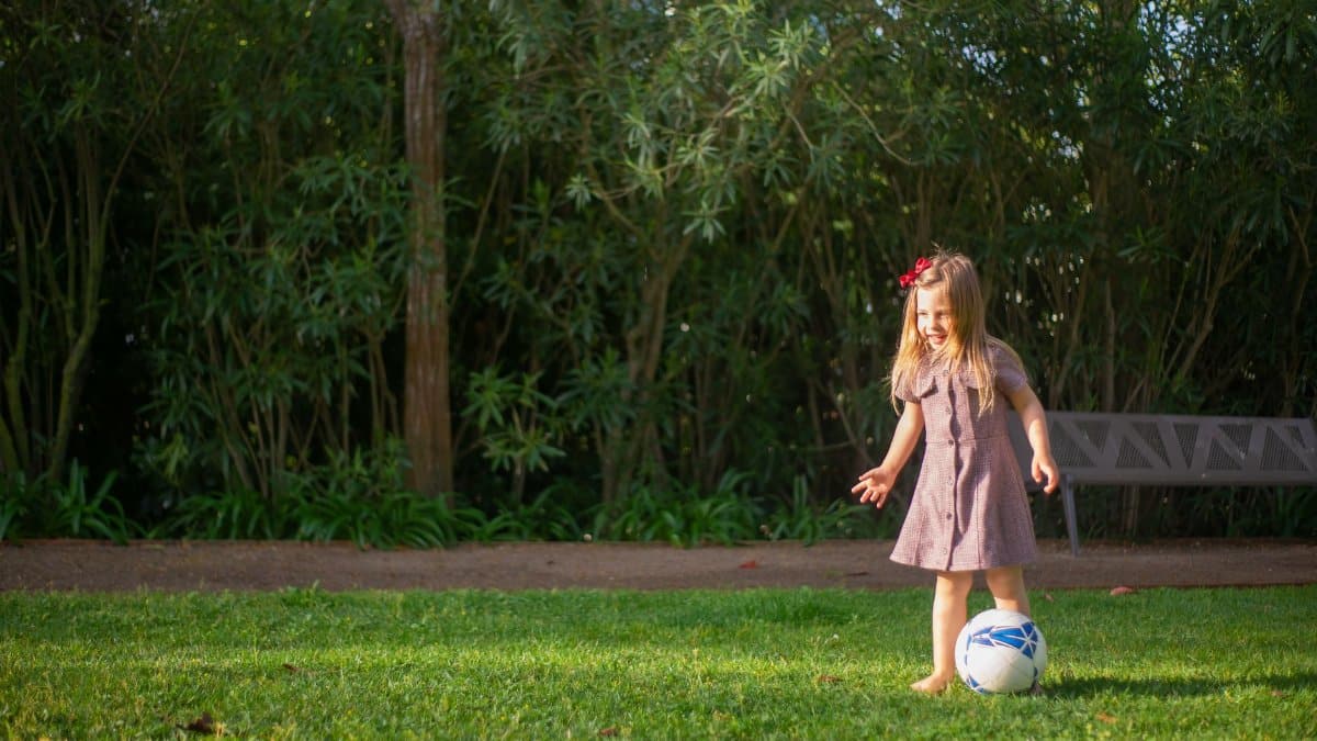 A cheerful young girl playing with a soccer ball on a sunny day in a Portuguese park.