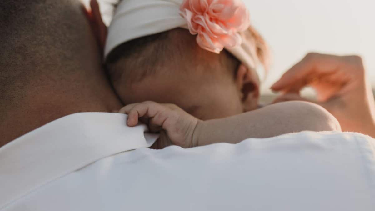 Tender close-up of a baby girl resting on her father's shoulder with a flower headband.