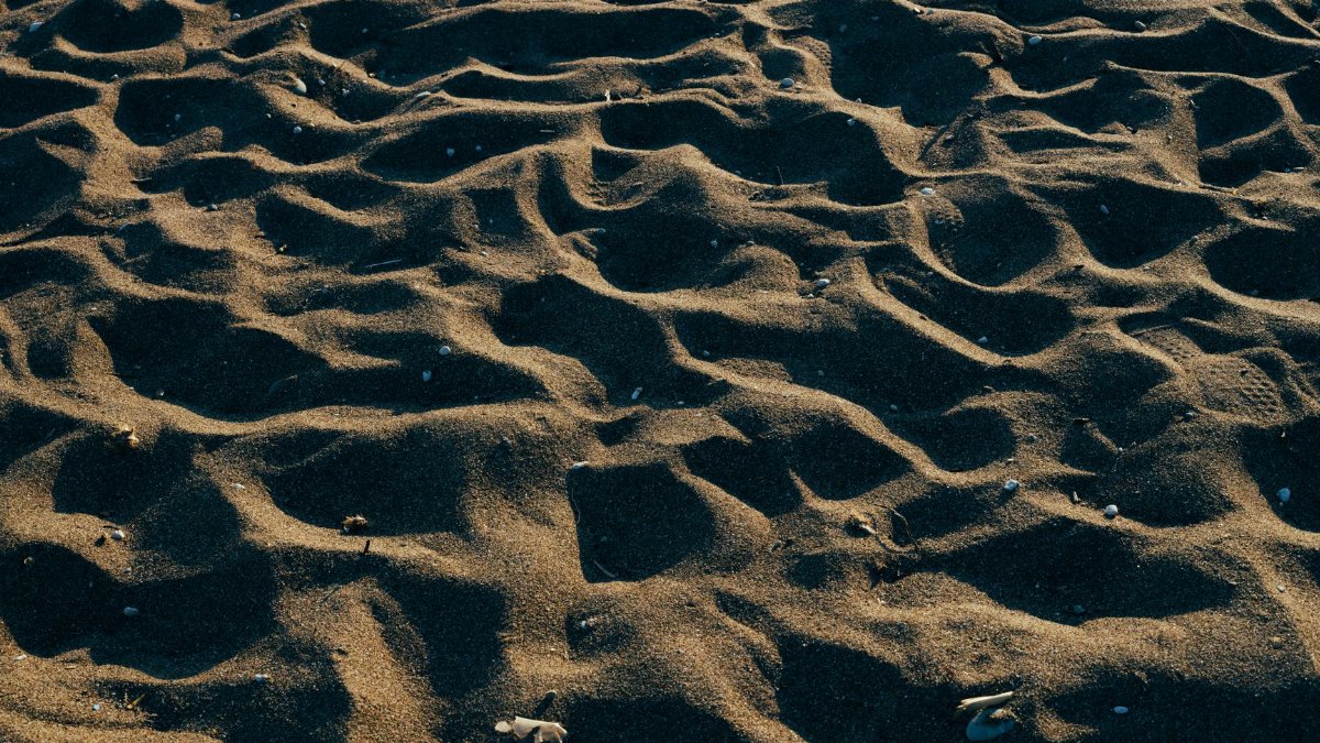 Close-up view of a sandy surface with intricate patterns created by natural light and shadow.