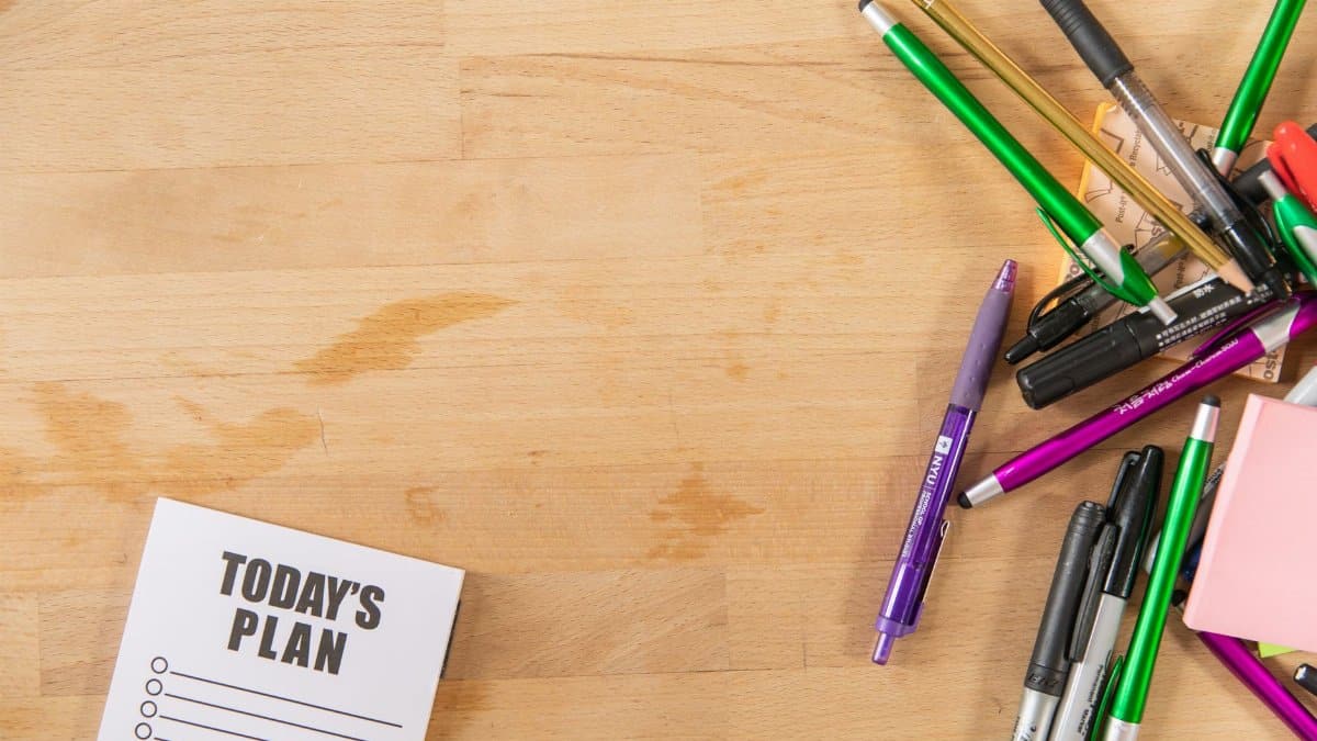 Flat lay of colorful pens, markers, and a notepad on a wooden surface with copy space.