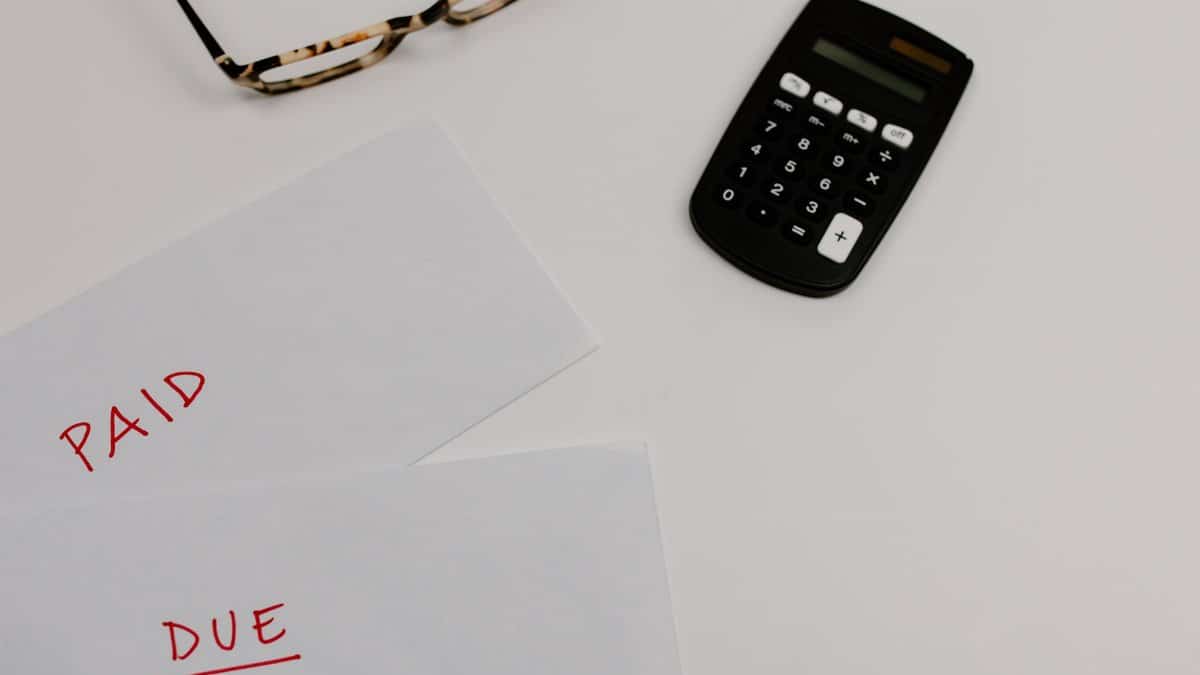 Top view of financial papers labeled 'Paid' and 'Due' beside a calculator and glasses.