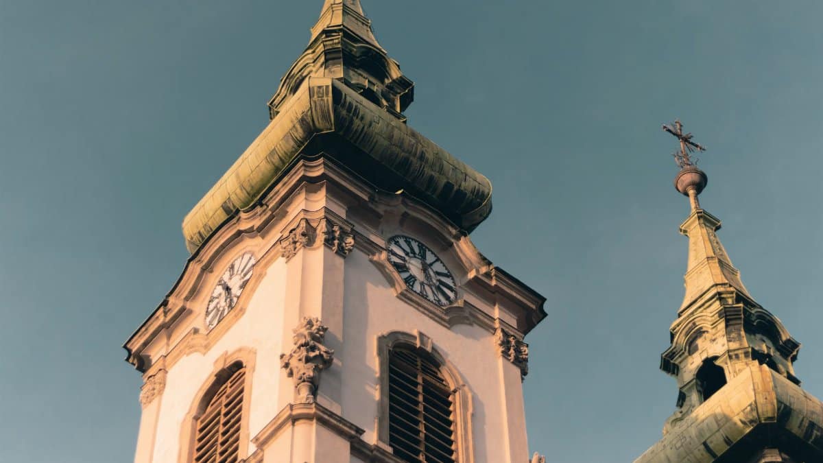 Low angle view of Gothic Revival church towers in Budapest, highlighting architectural details and clock faces.