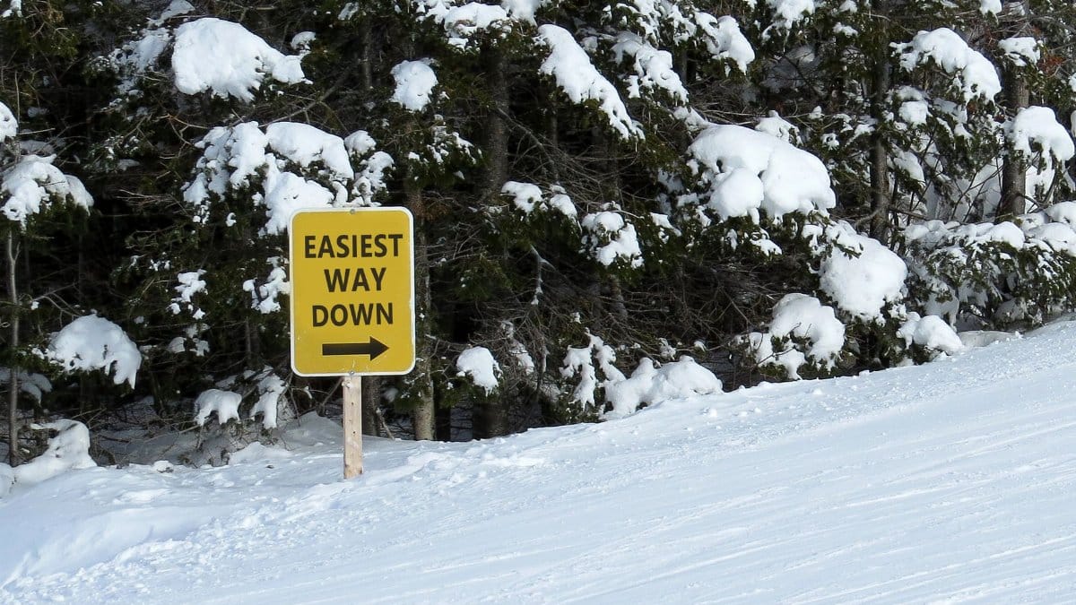 Snow-covered ski trail with a sign reading 'Easiest Way Down' indicating direction in a forest setting.