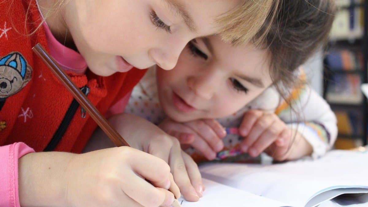 Two young girls focus on a drawing project together, sharing creativity and learning.