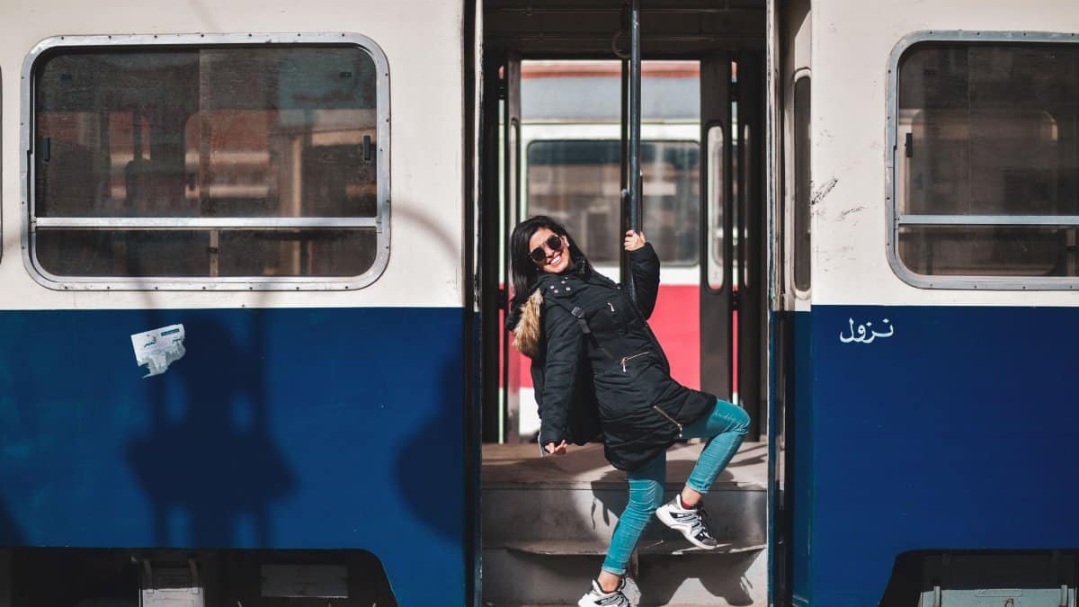 A woman joyfully poses on a train's step, showcasing a vibrant travel moment.