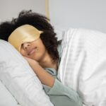 A woman with afro hair sleeps soundly in bed with a sleep mask, enjoying a cozy indoor atmosphere.