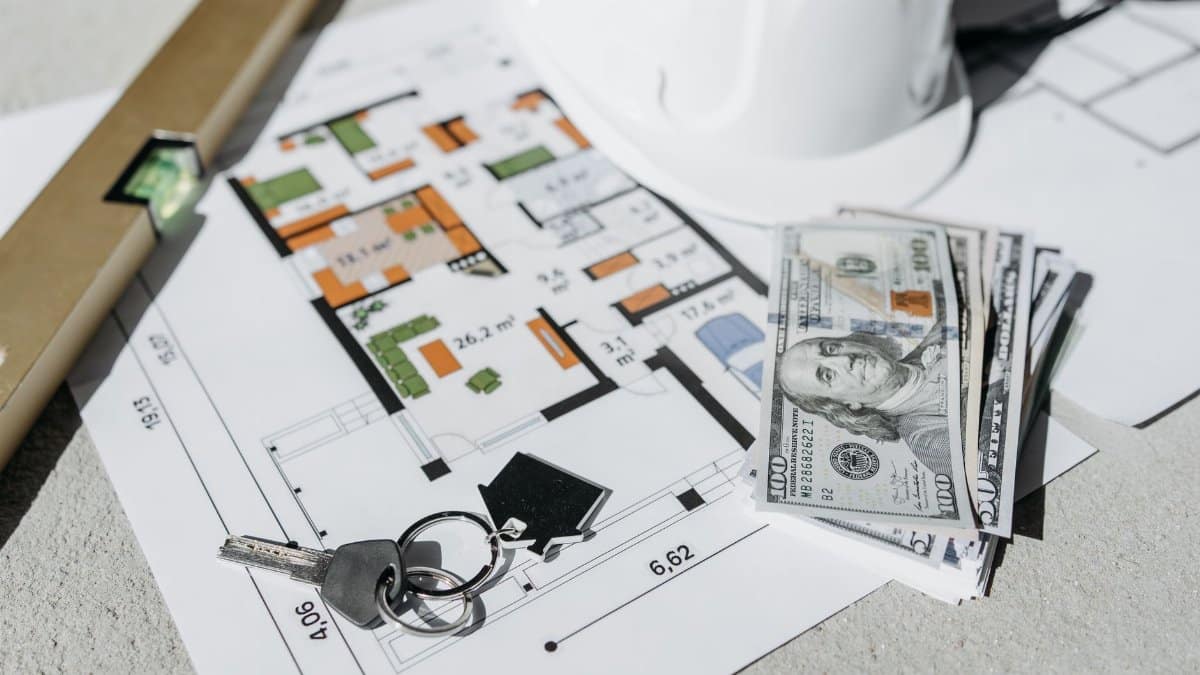 Floor plan with cash, keys, and hard hat symbolizing real estate investment and property planning.