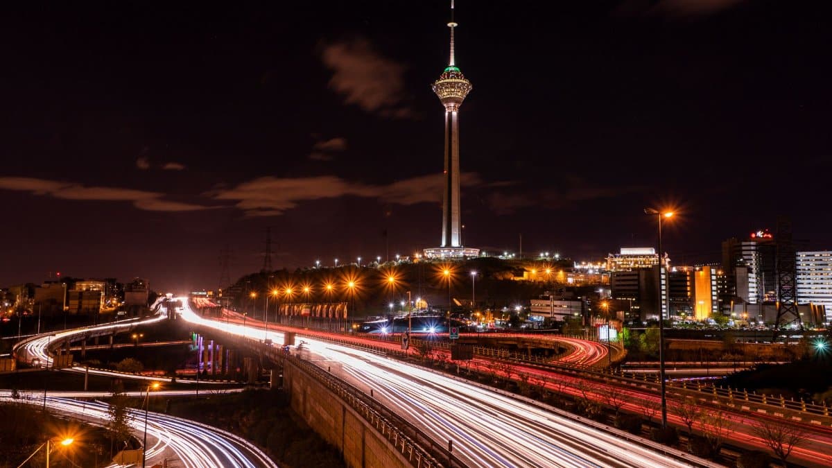 Stunning night view of Tehran's Milad Tower with light streaks from highway traffic.