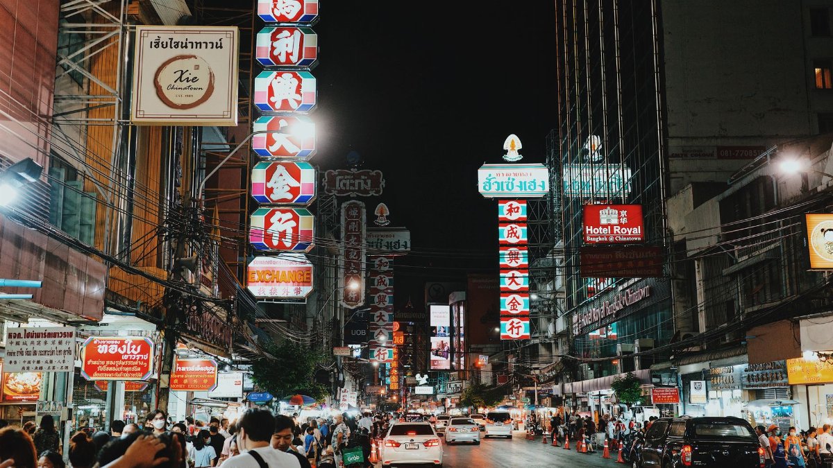 Bustling night scene in Bangkok's Chinatown with illuminated signs, people, and traffic.