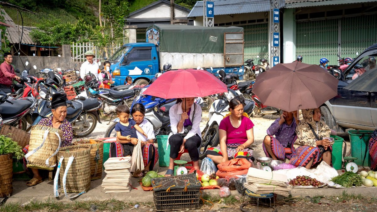 A vibrant rural market with local vendors selling fresh produce and goods under umbrellas.