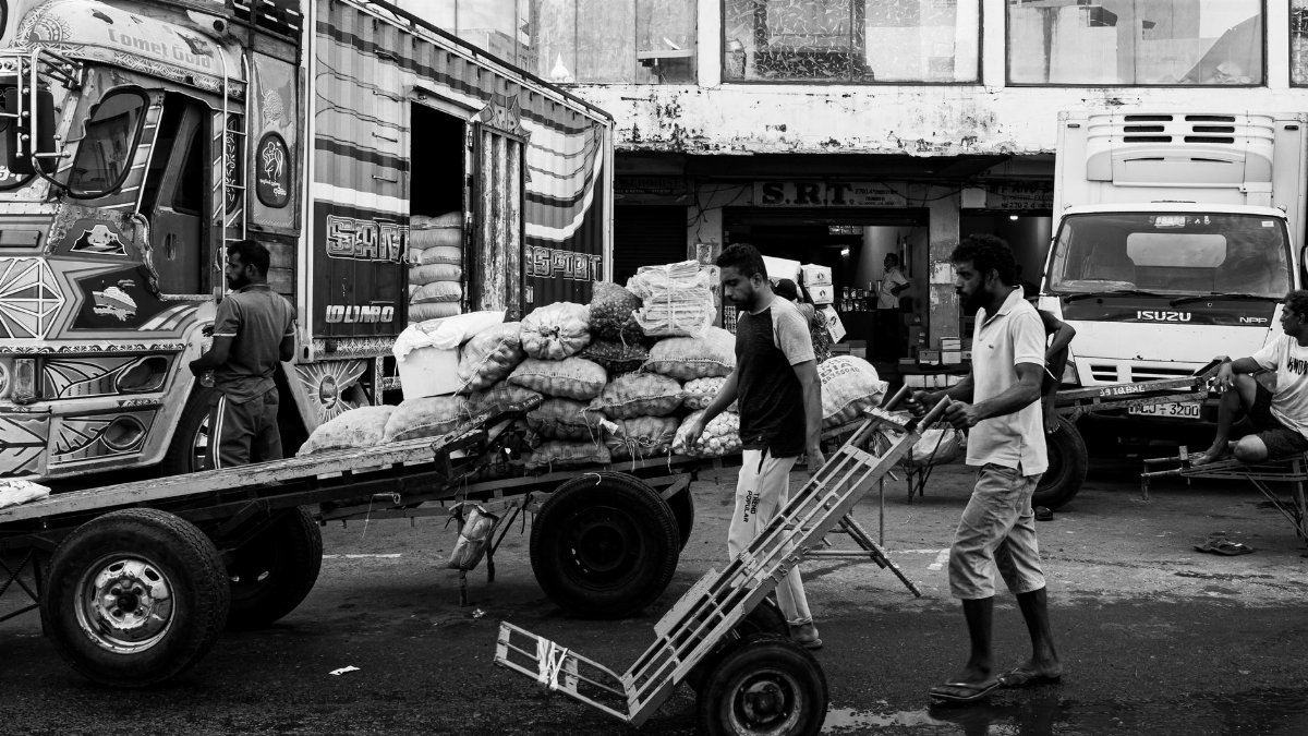 Black and white street market scene in Colombo, Sri Lanka with workers loading trucks.