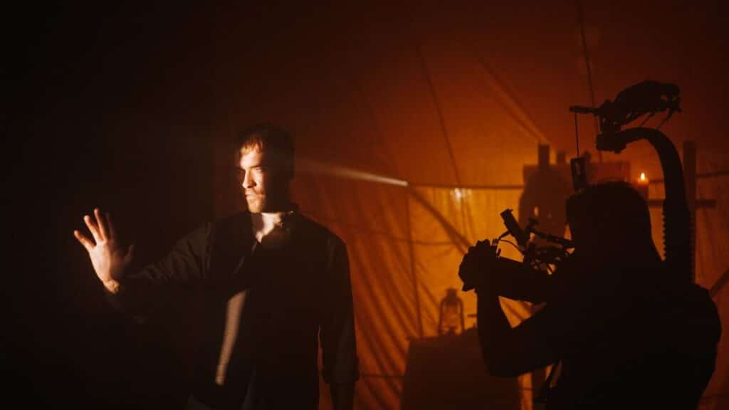 A man on a film set with dramatic lighting, facing a cinematographer.