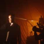 A man on a film set with dramatic lighting, facing a cinematographer.