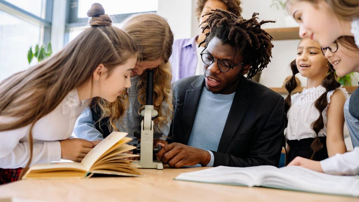 Students and teacher engage in science lesson using a microscope, fostering curiosity and learning.