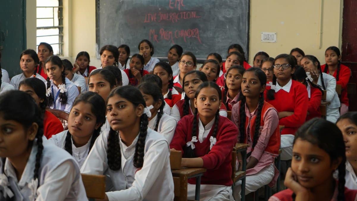 Group of Indian schoolgirls in uniform attentively listening in a classroom setting.