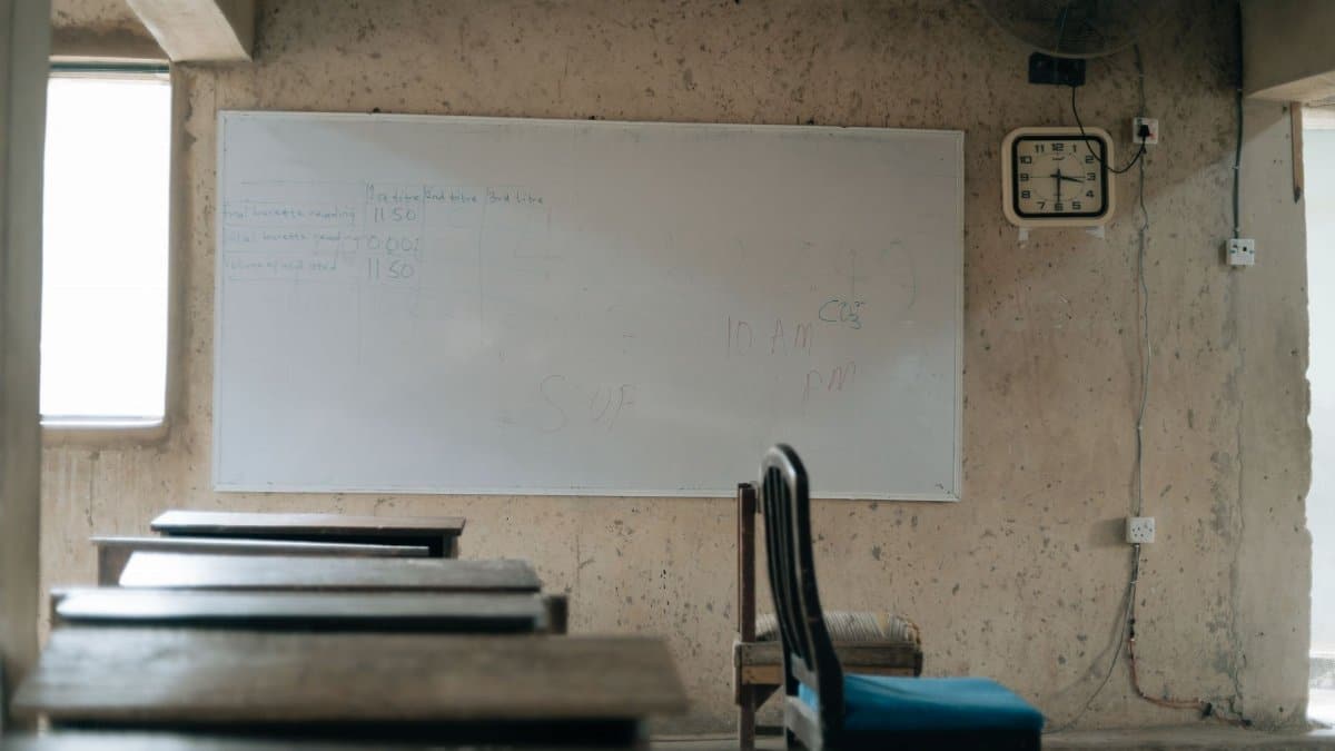 An empty classroom featuring old wooden desks, a whiteboard, and a wall clock, highlighting education.