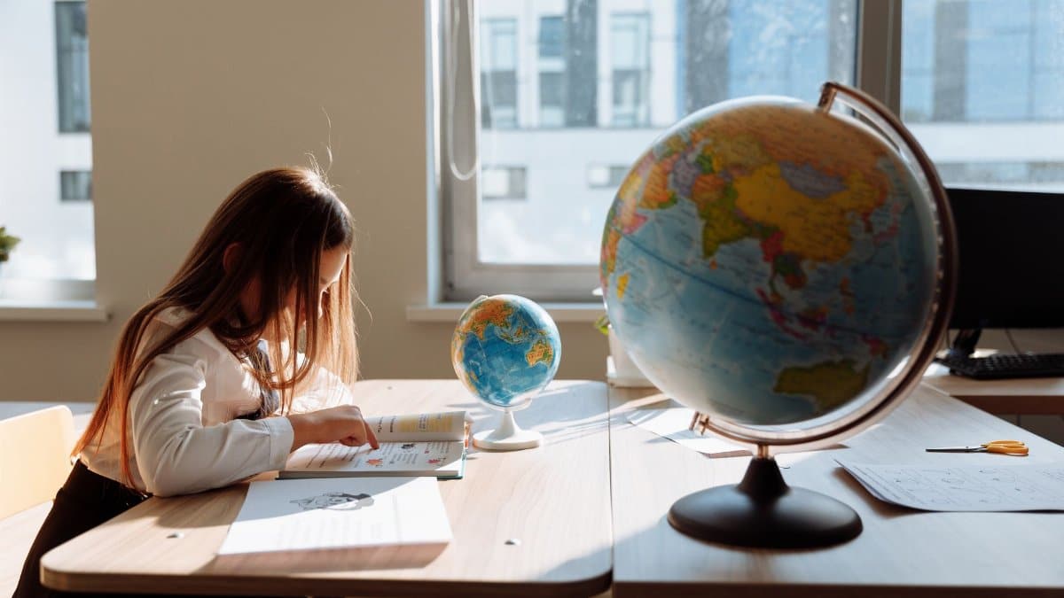 A young girl diligently studying in a sunlit classroom with a globe and books.