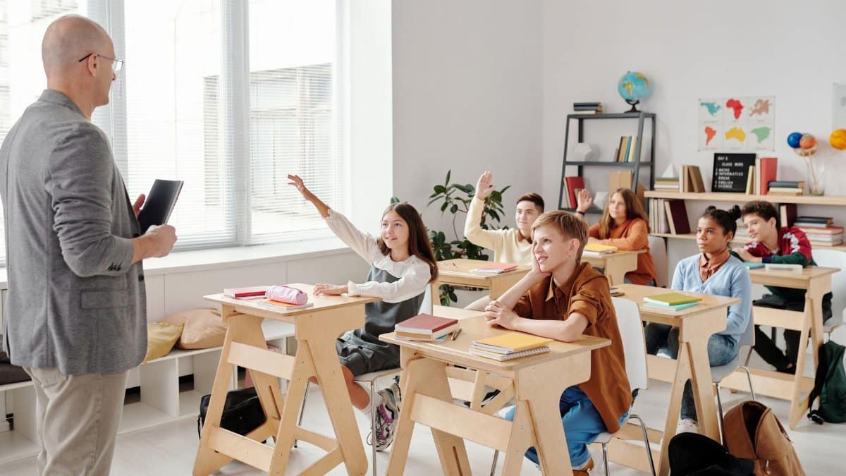Students engage eagerly in a classroom, raising hands and participating in a lesson with their teacher.