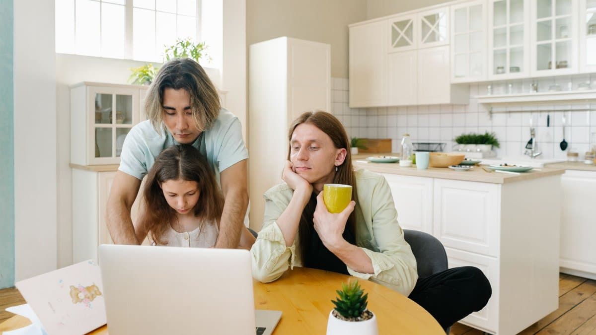 A family spends quality time together in a modern kitchen, focused on a laptop.