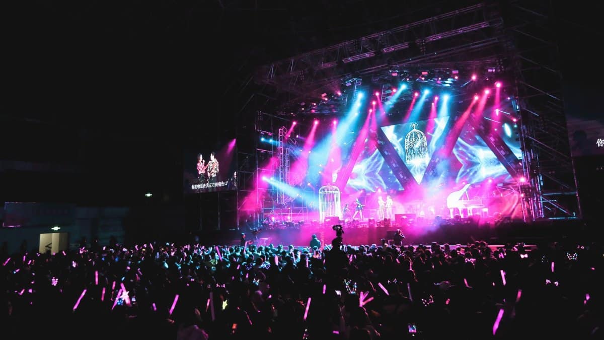 Unrecognizable musicians performing on concert hall stage illuminated by colorful spotlights in front of public in evening