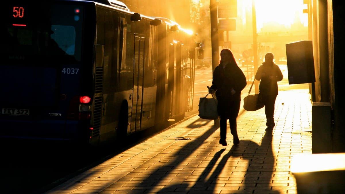 Silhouettes of commuters walking beside a bus during sunrise on a street in Stockholm, Sweden.