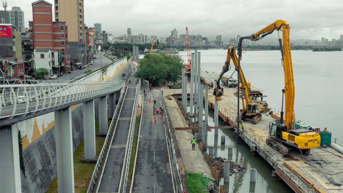 Aerial view of a construction site along a riverfront in Taipei, Taiwan, with machinery and workers.