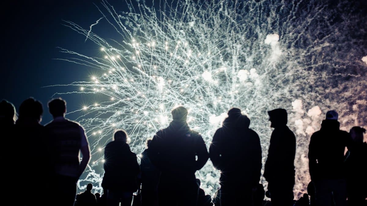 Silhouetted crowd watching a dazzling fireworks display at night, creating a vibrant and festive atmosphere.