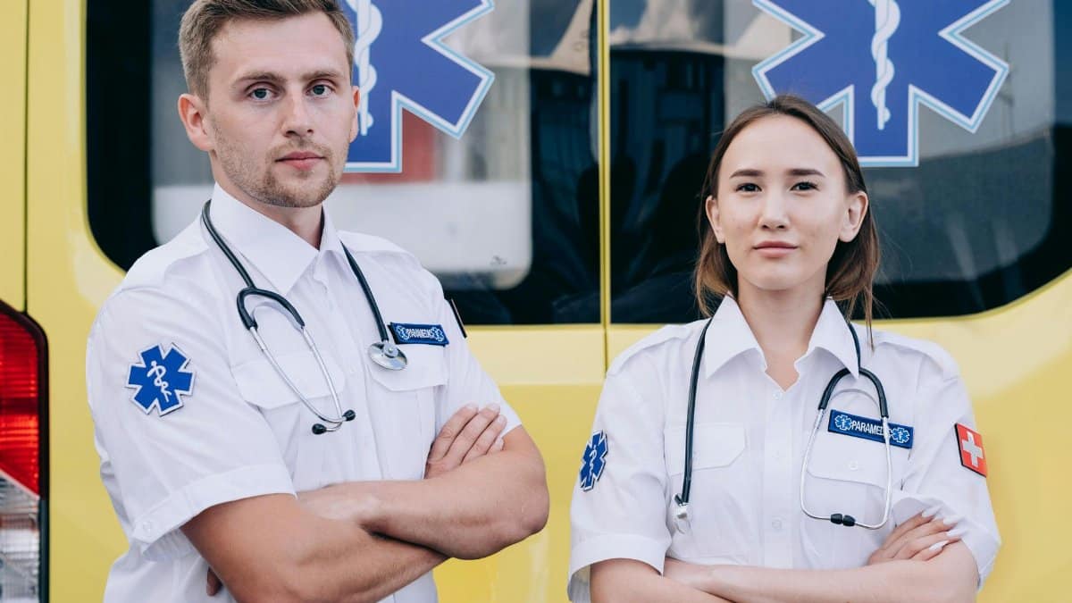 Portrait of two paramedics with stethoscopes standing confidently in front of an ambulance.